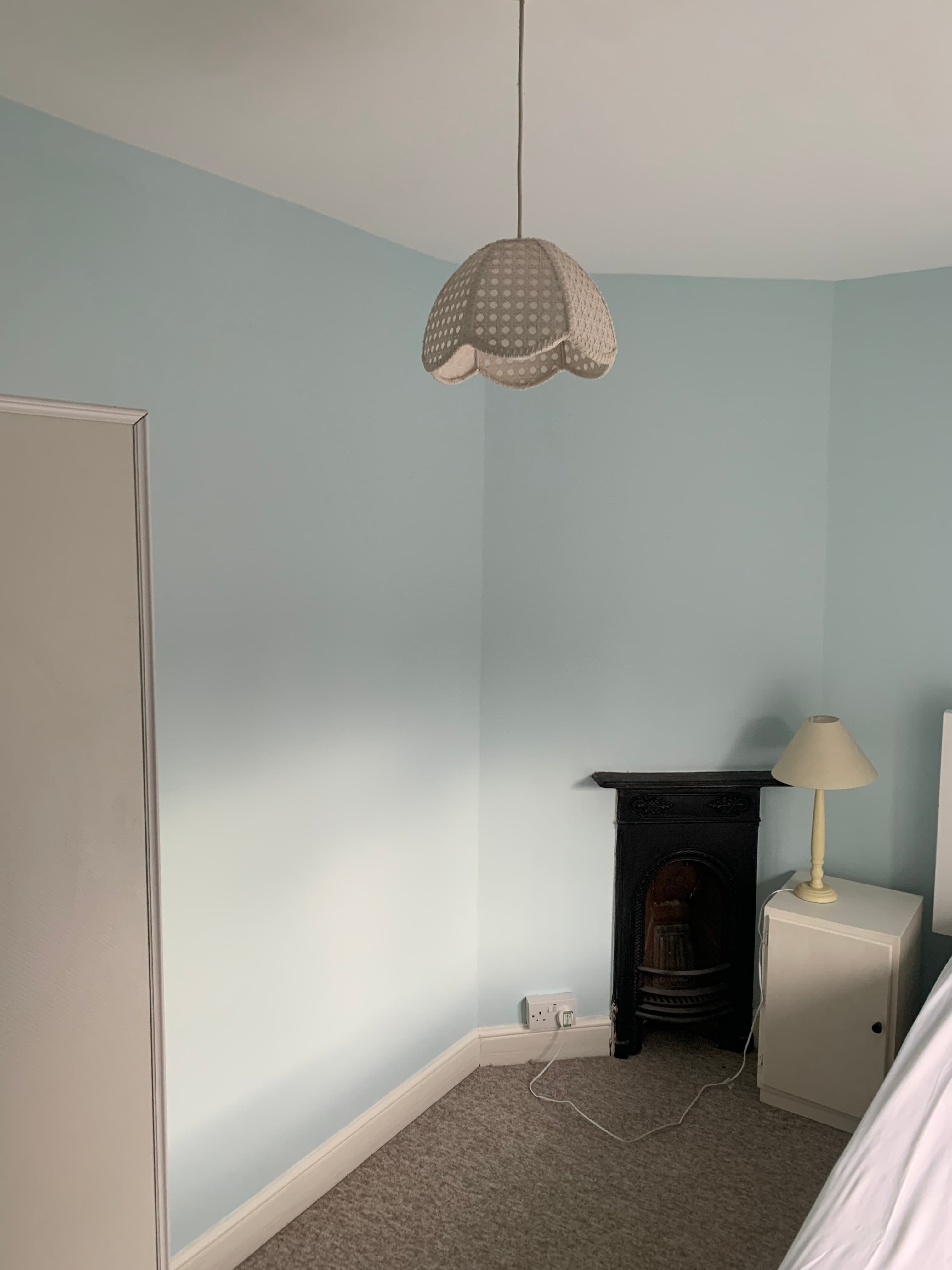 Light blue room corner with a scalloped pendant light, vintage fireplace, and white bedside table.