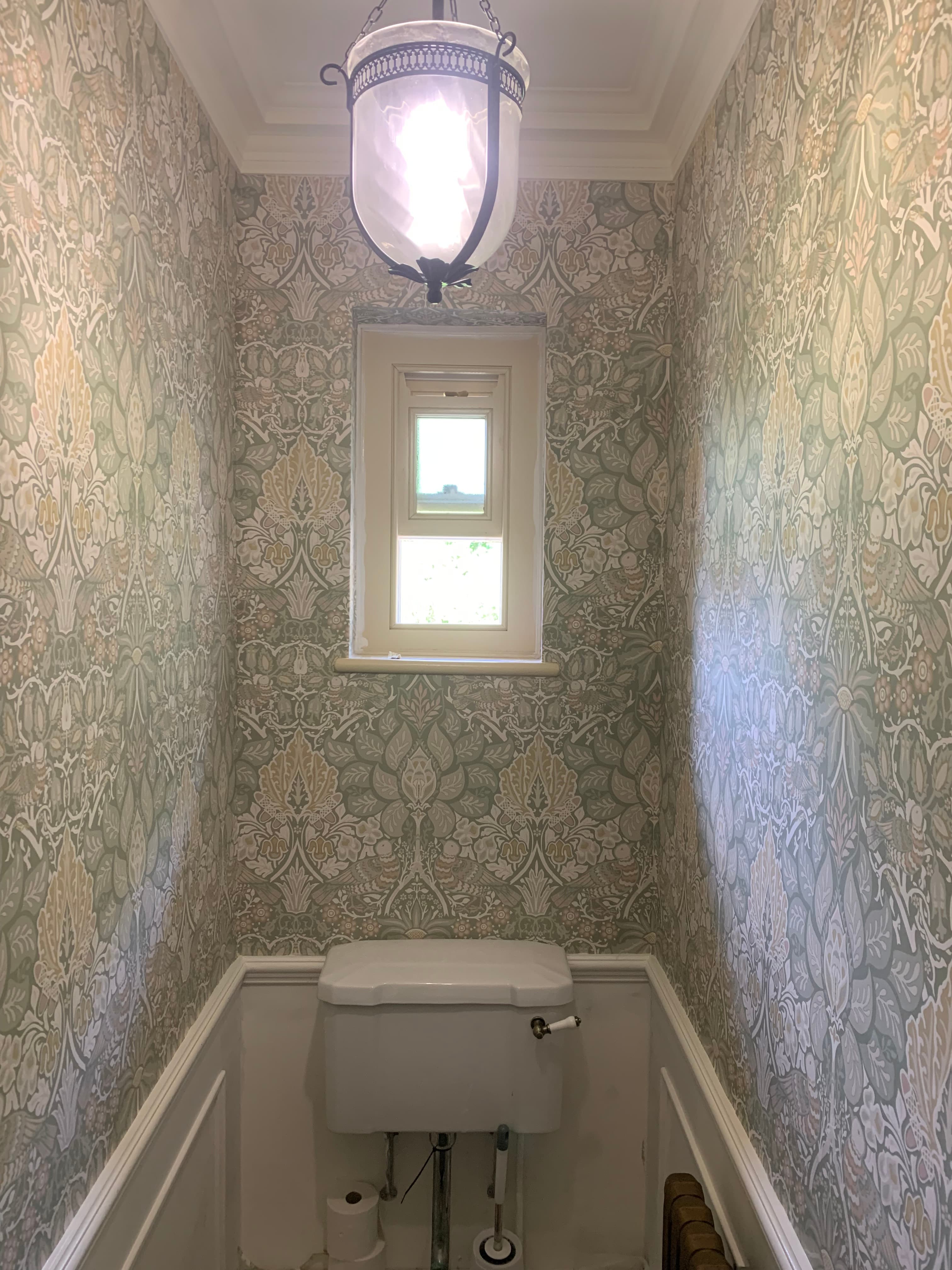 Small bathroom featuring intricate floral wallpaper, a central window, and a glass pendant light.